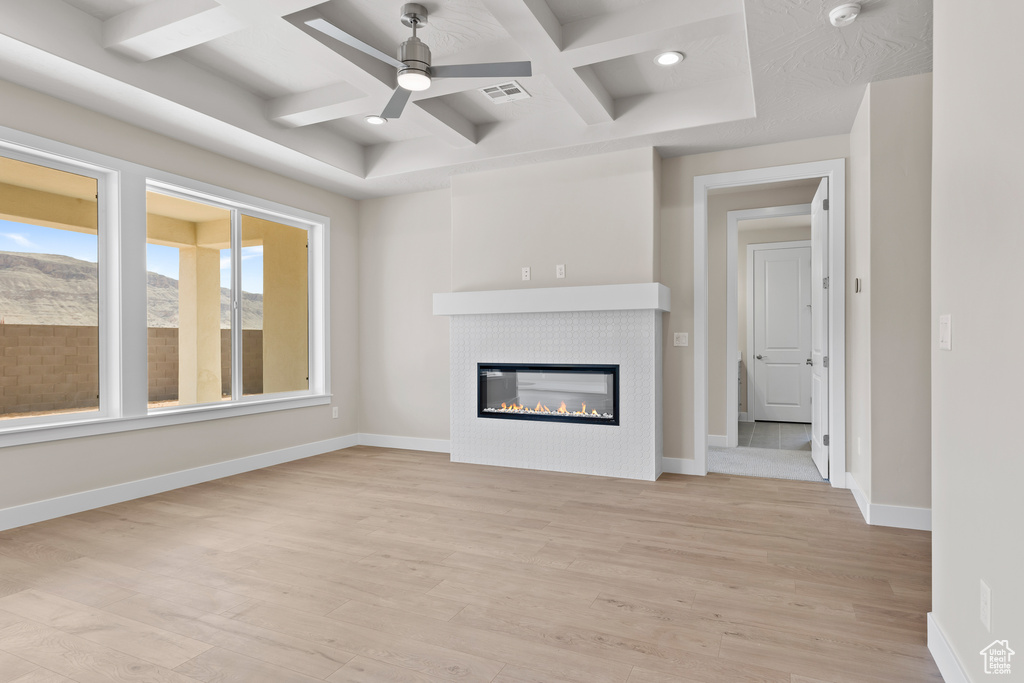 Unfurnished living room with coffered ceiling, a ceiling fan, light wood finished floors, a tile fireplace, and baseboards
