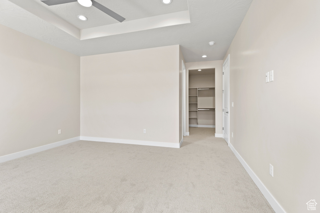 Unfurnished room featuring light colored carpet, a ceiling fan, recessed lighting, baseboards, and a raised ceiling