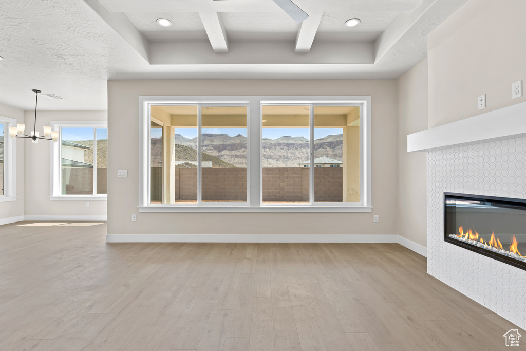 Unfurnished living room with wood finished floors, a mountain view, a tiled fireplace, a chandelier, and baseboards