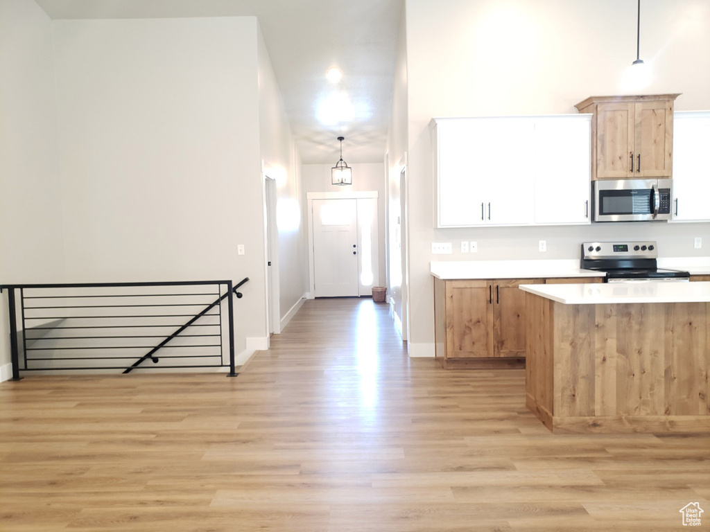 Kitchen with stainless steel appliances, light wood finished floors, light countertops, hanging light fixtures, and baseboards