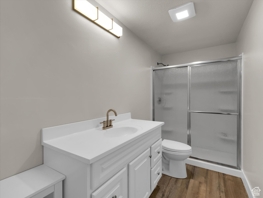 Bathroom with a stall shower, wood finished floors, toilet, and vanity