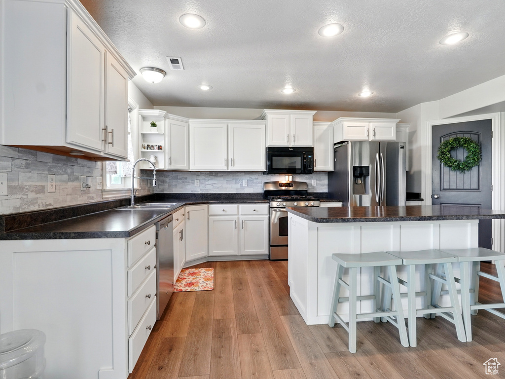 Kitchen with appliances with stainless steel finishes, a sink, open shelves, white cabinets, and recessed lighting