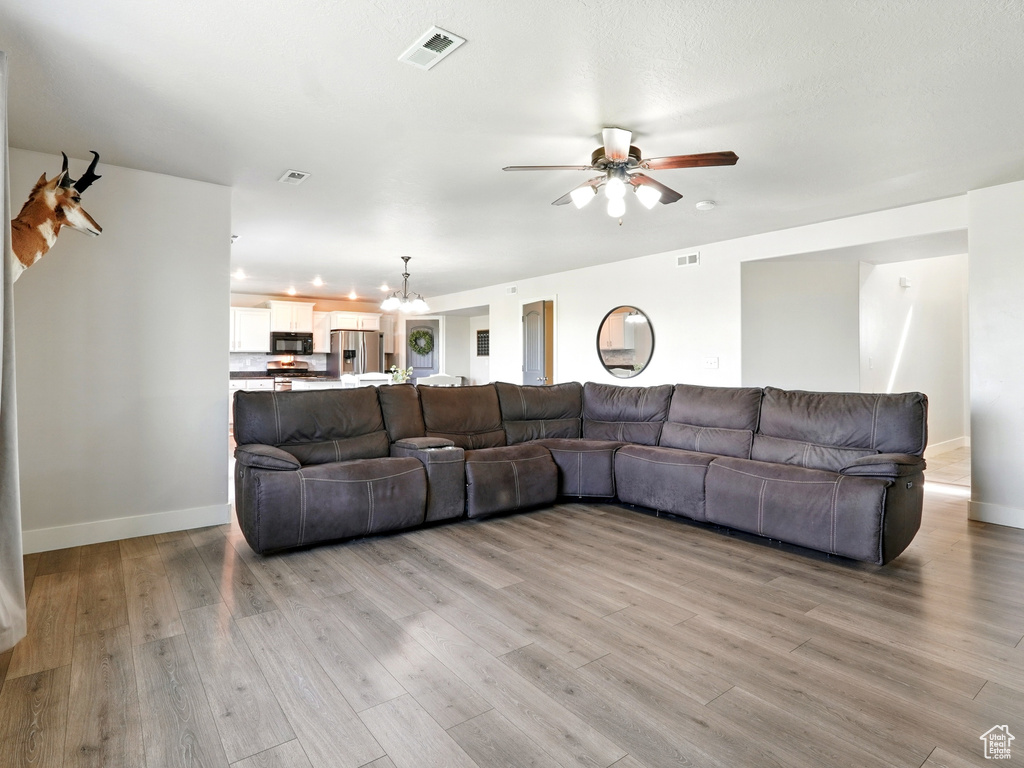 Living area with ceiling fan, light wood-type flooring, a chandelier, and baseboards