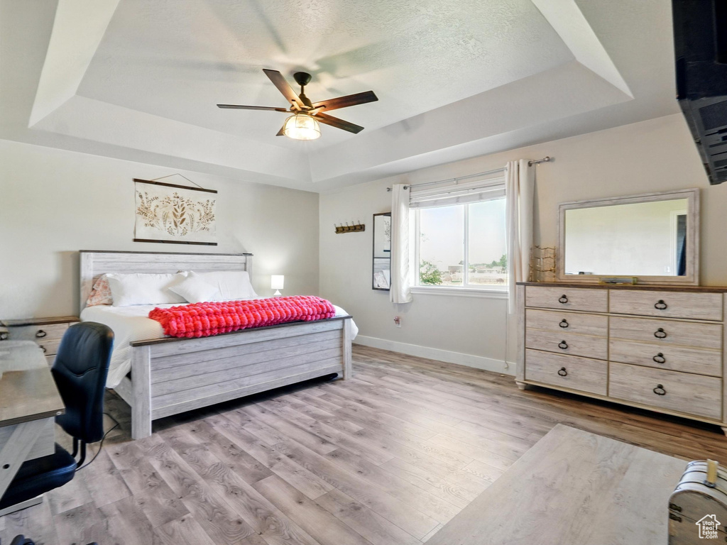 Bedroom with a raised ceiling, light wood finished floors, baseboards, and ceiling fan