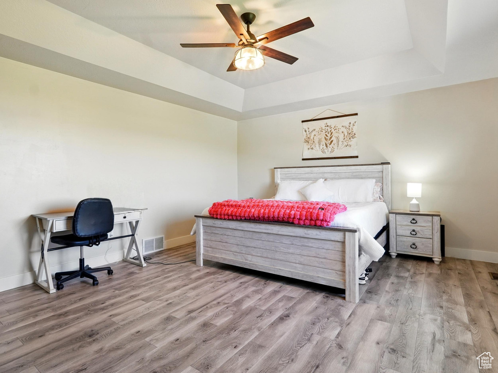 Bedroom featuring a raised ceiling, wood finished floors, baseboards, and ceiling fan