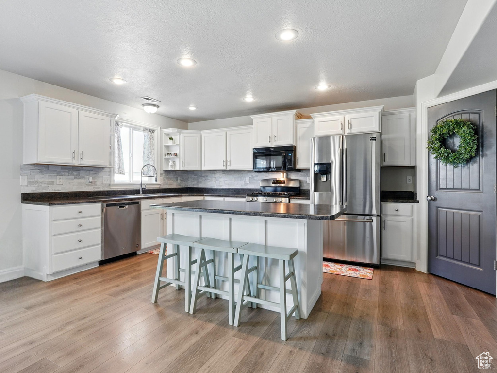 Kitchen with appliances with stainless steel finishes, a sink, white cabinets, backsplash, and a textured ceiling