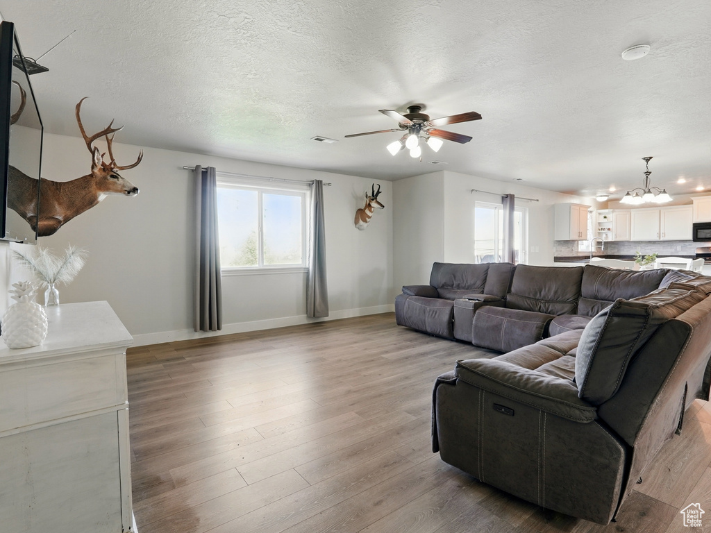 Living room with a chandelier, baseboards, ceiling fan, light wood-style flooring, and a textured ceiling