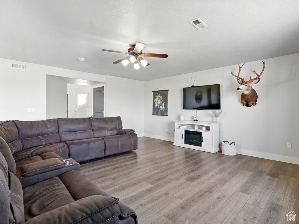 Living area with a ceiling fan, light wood-style floors, baseboards, and a glass covered fireplace