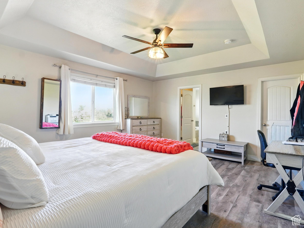 Bedroom featuring a tray ceiling, wood finished floors, connected bathroom, and a ceiling fan