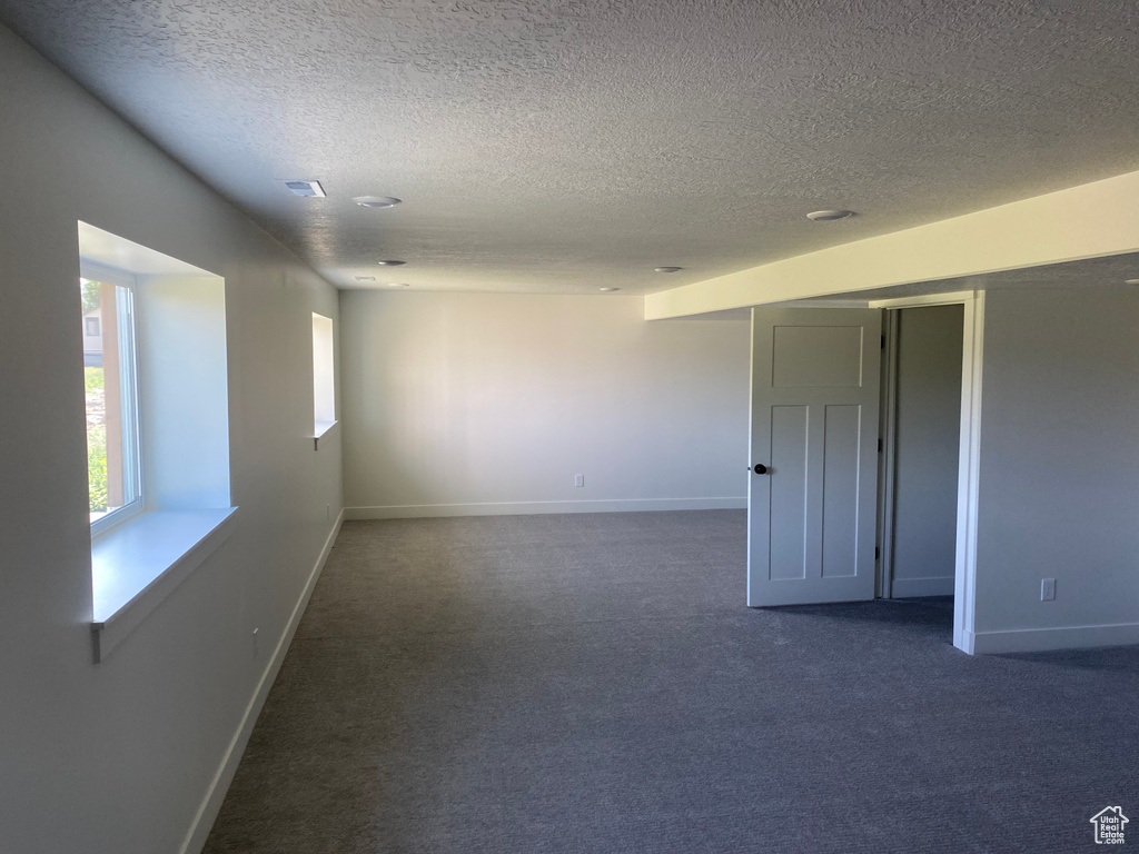 Empty room with a textured ceiling, dark colored carpet, and baseboards
