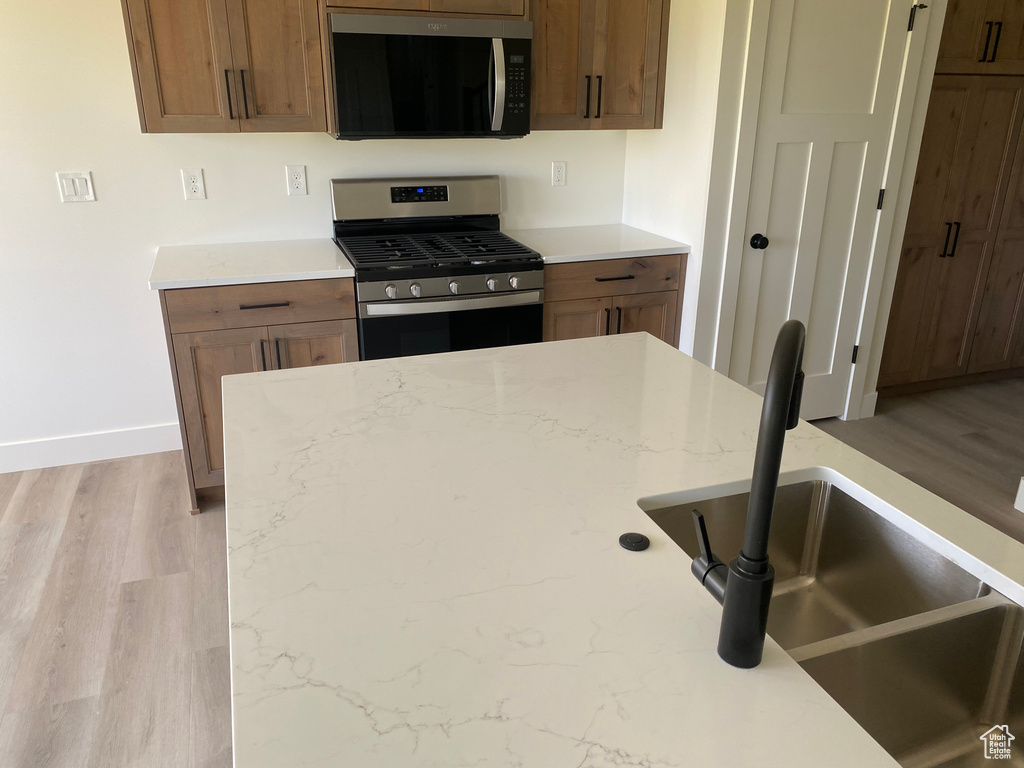 Kitchen featuring stainless steel gas range oven, a sink, baseboards, and light wood-style floors