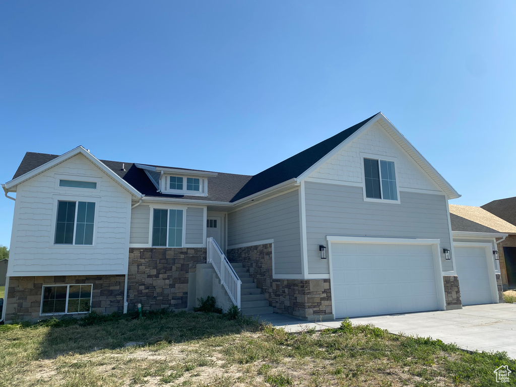 View of front of property featuring stone siding, a garage, driveway, and roof with shingles