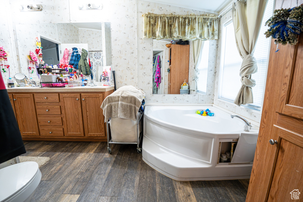 Bathroom featuring wallpapered walls, wood finished floors, a bath, vanity, and toilet