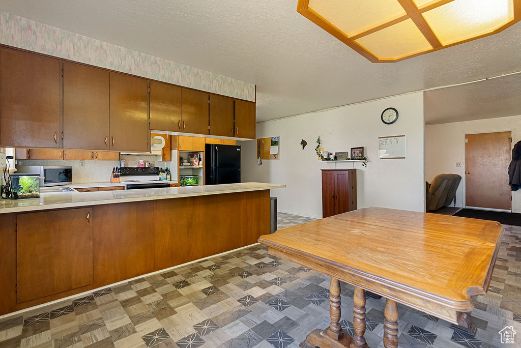 Kitchen featuring white range with electric stovetop, freestanding refrigerator, a peninsula, light countertops, and stainless steel microwave