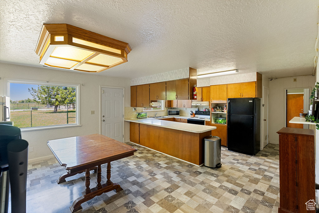 Kitchen with freestanding refrigerator, electric range, a peninsula, light countertops, and brown cabinets