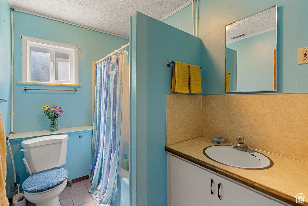 Bathroom with a textured ceiling, toilet, vanity, tile patterned flooring, and shower / tub combo with curtain