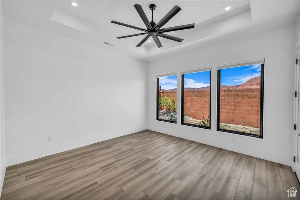 Spare room featuring wood finished floors, a raised ceiling, baseboards, a ceiling fan, and recessed lighting