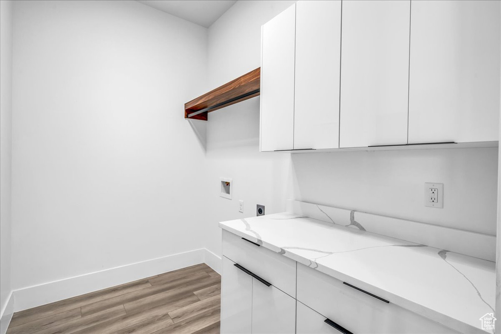 Laundry area featuring electric dryer hookup, hookup for a washing machine, light wood-type flooring, baseboards, and cabinet space