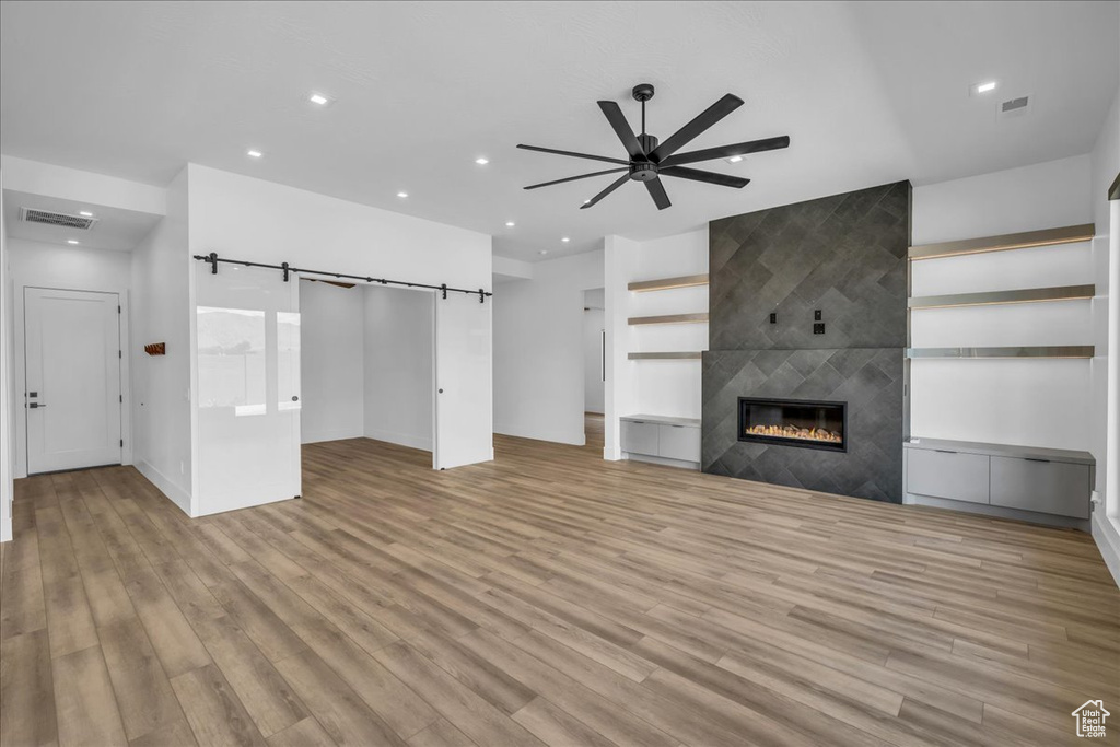 Unfurnished living room with ceiling fan, light wood-style flooring, recessed lighting, a tile fireplace, and a barn door
