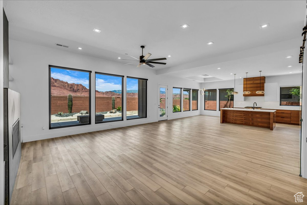 Unfurnished living room featuring a sink, a ceiling fan, light wood finished floors, recessed lighting, and baseboards