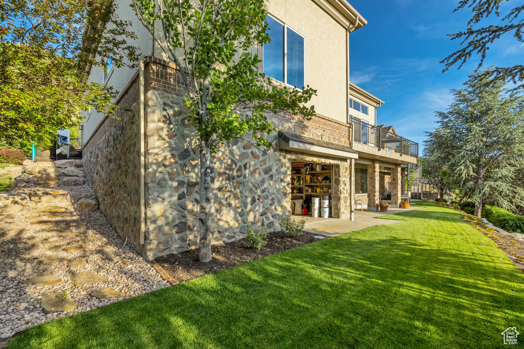 Rear view of property featuring a balcony, a yard, stone siding, and a patio area