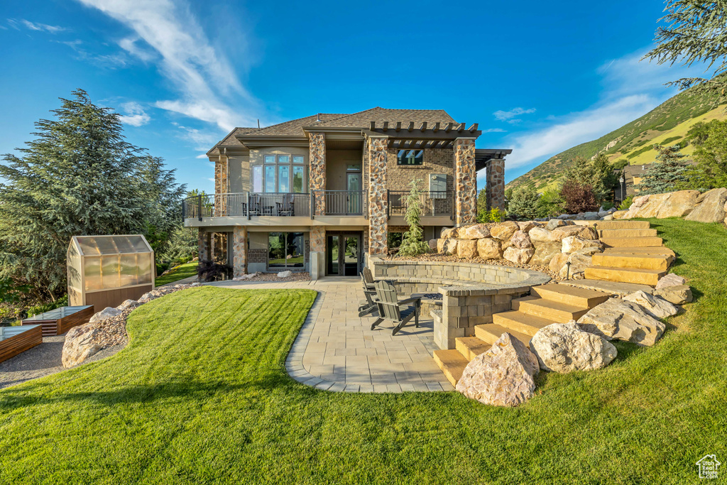 Rear view of house with a balcony, a greenhouse, a yard, and a patio area