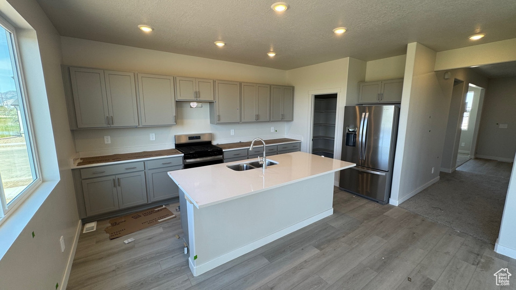 Kitchen with gray cabinets, stainless steel refrigerator with ice dispenser, gas stove, a sink, and a textured ceiling