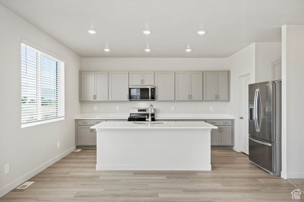 Kitchen with stainless steel appliances, gray cabinets, a kitchen island with sink, light countertops, and recessed lighting