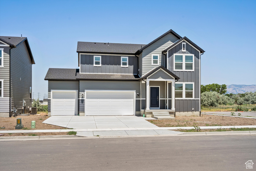 View of front of house with board and batten siding, driveway, an attached garage, and a shingled roof