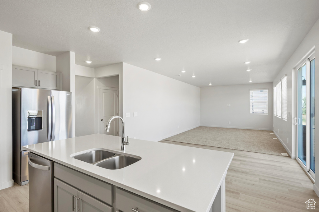 Kitchen with dishwasher, light countertops, an island with sink, light wood-style flooring, and open floor plan