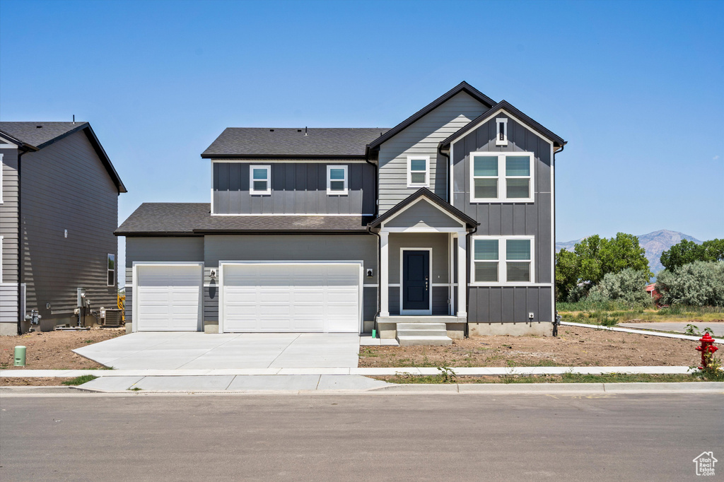 View of front of home with board and batten siding, driveway, an attached garage, and roof with shingles
