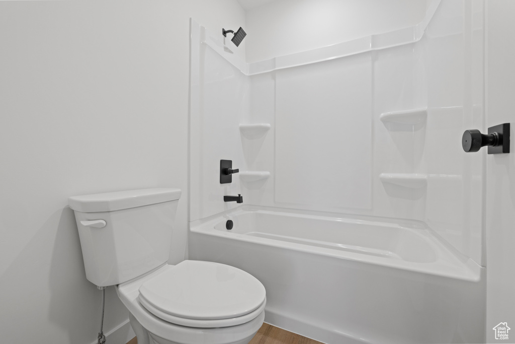 Full bathroom with bathtub / shower combination, toilet, and wood finished floors