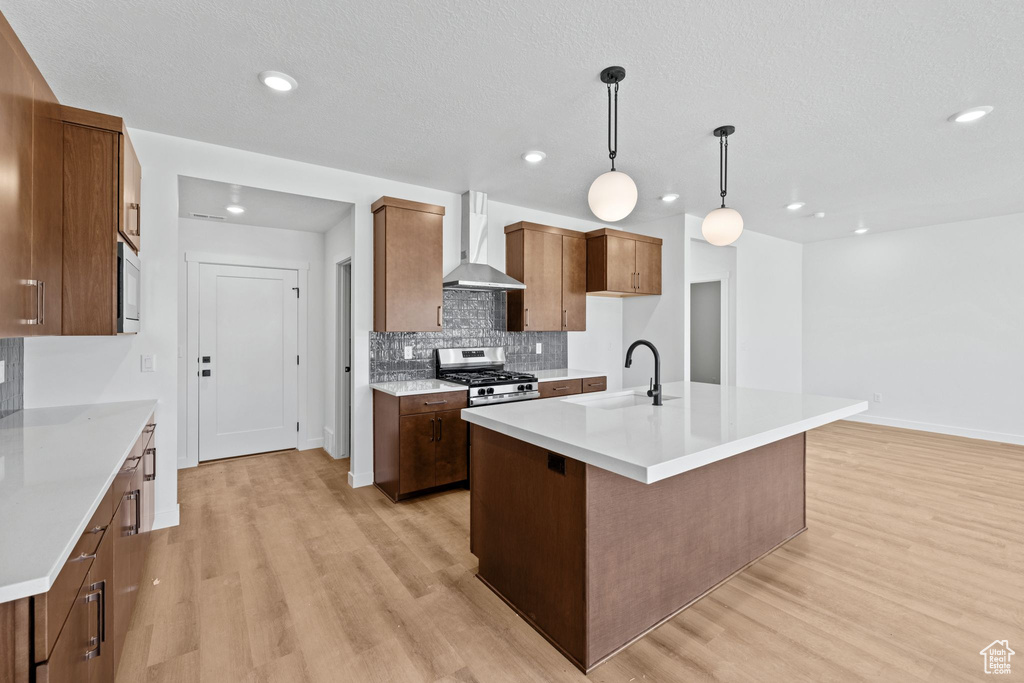 Kitchen featuring wall chimney exhaust hood, a sink, stainless steel range with gas stovetop, light wood-type flooring, and recessed lighting