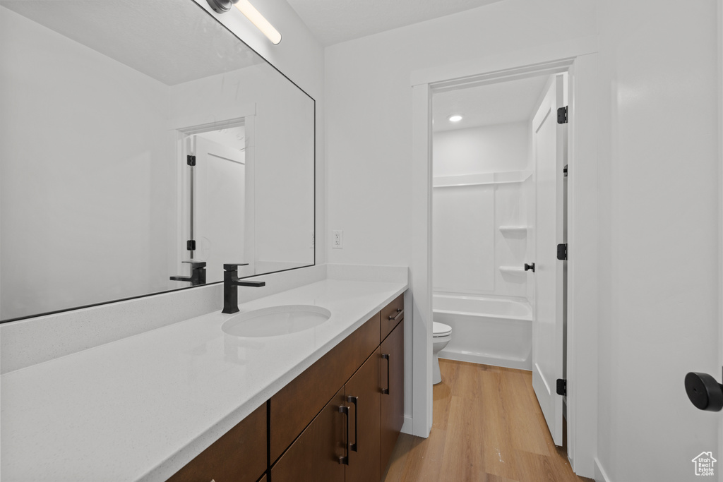 Full bath featuring toilet, vanity, wood finished floors, and shower / tub combination