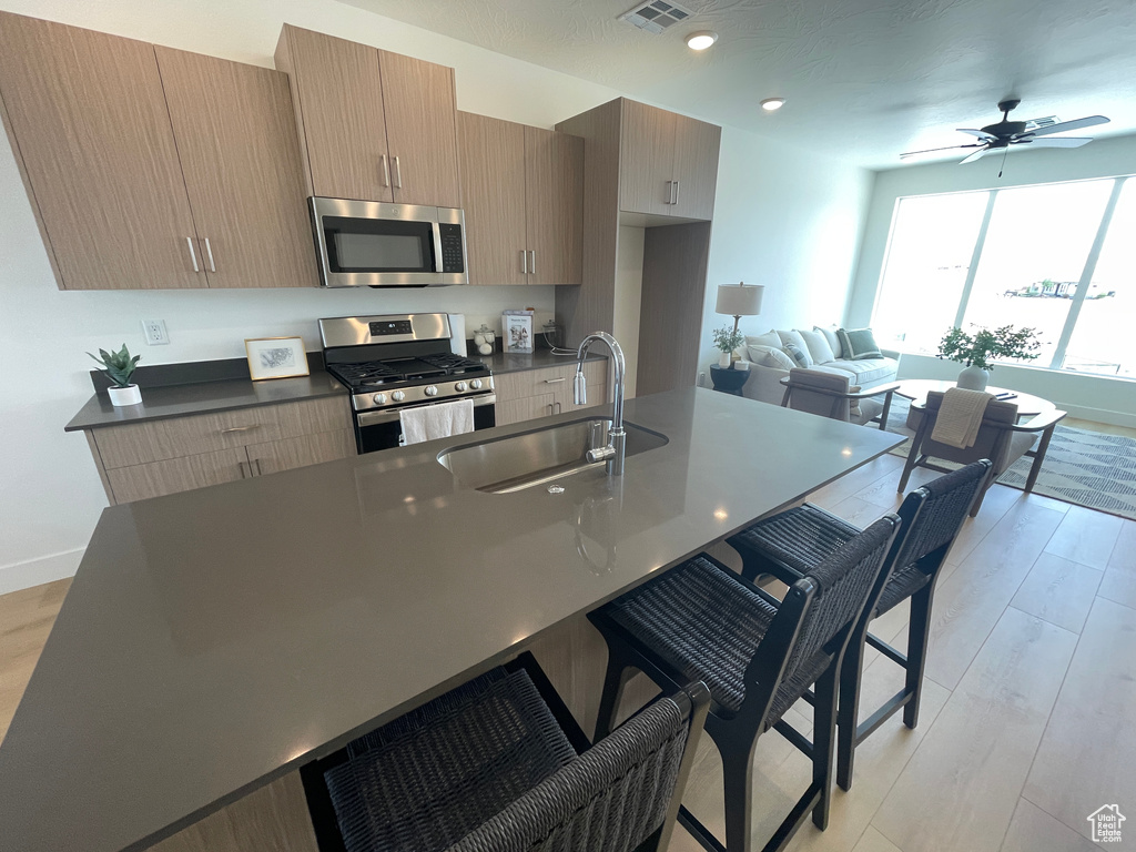 Kitchen featuring stainless steel appliances, a sink, dark countertops, a kitchen breakfast bar, and light wood-style flooring