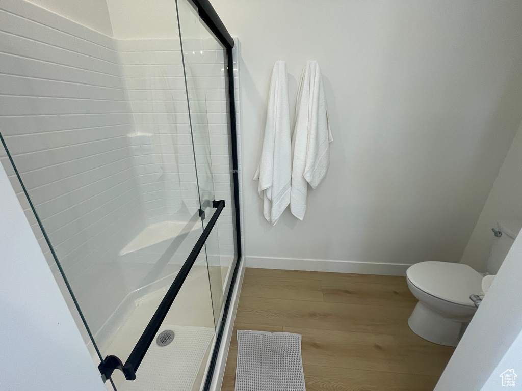 Bathroom featuring wood finished floors, a stall shower, toilet, and baseboards