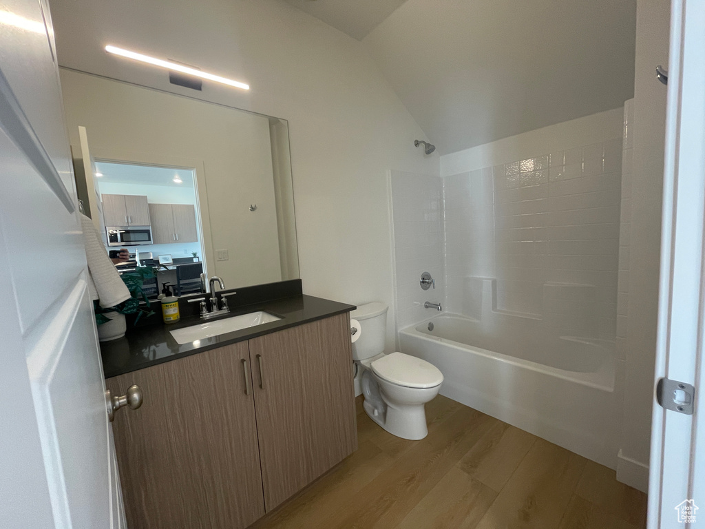 Bathroom with wood finished floors, toilet, vanity, vaulted ceiling, and shower / bathtub combination
