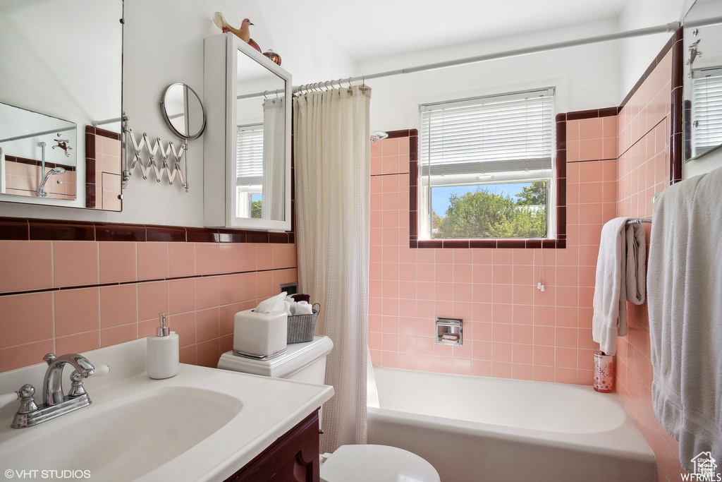 Bathroom featuring shower / bath combination with curtain, tile walls, vanity, and toilet