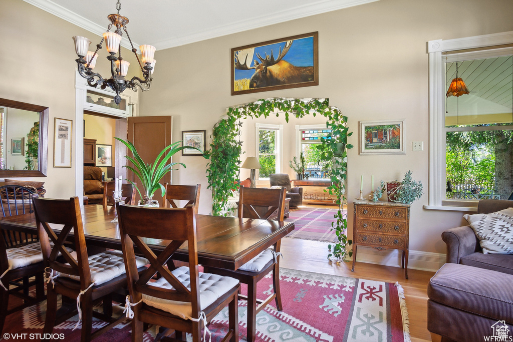 Dining area featuring healthy amount of natural light, crown molding, wood finished floors, a chandelier, and baseboards