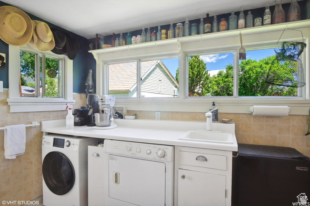 Kitchen with washer and dryer, healthy amount of natural light, white cabinetry, and a sink