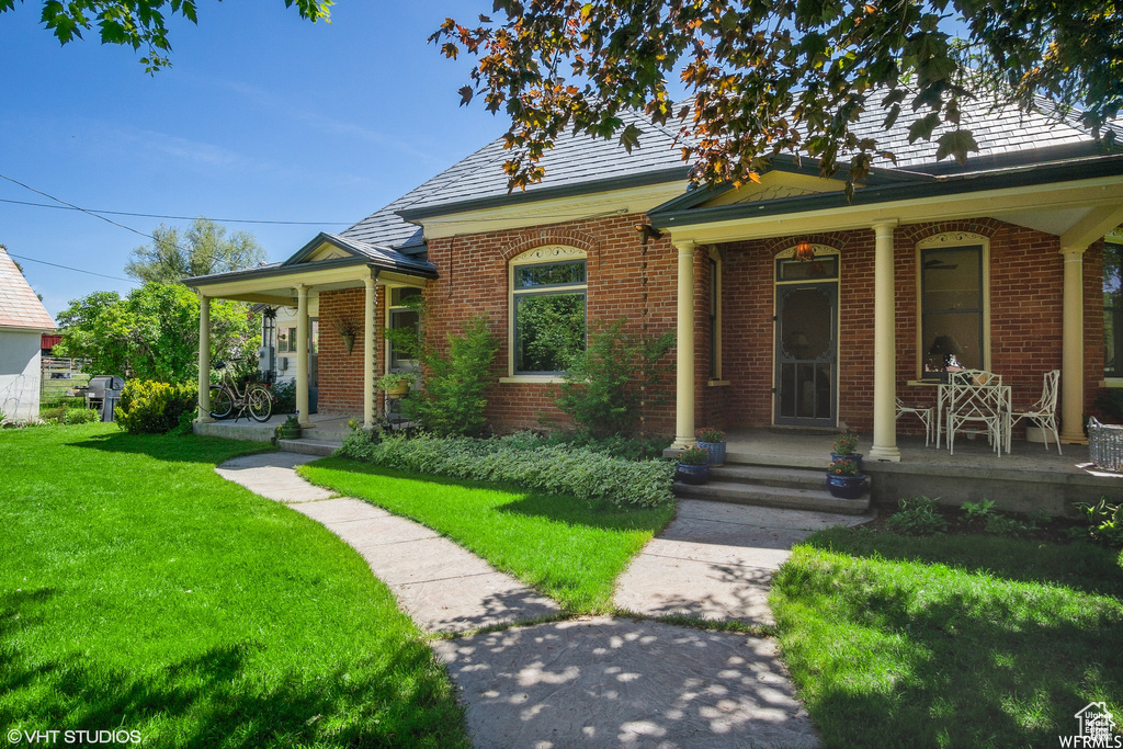 View of front facade featuring covered porch, brick siding, a front lawn, and a high end roof