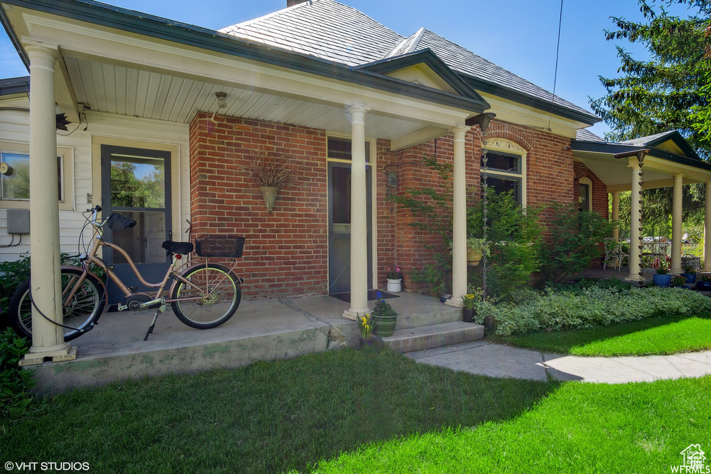 Entrance to property with brick siding, a porch, and a yard