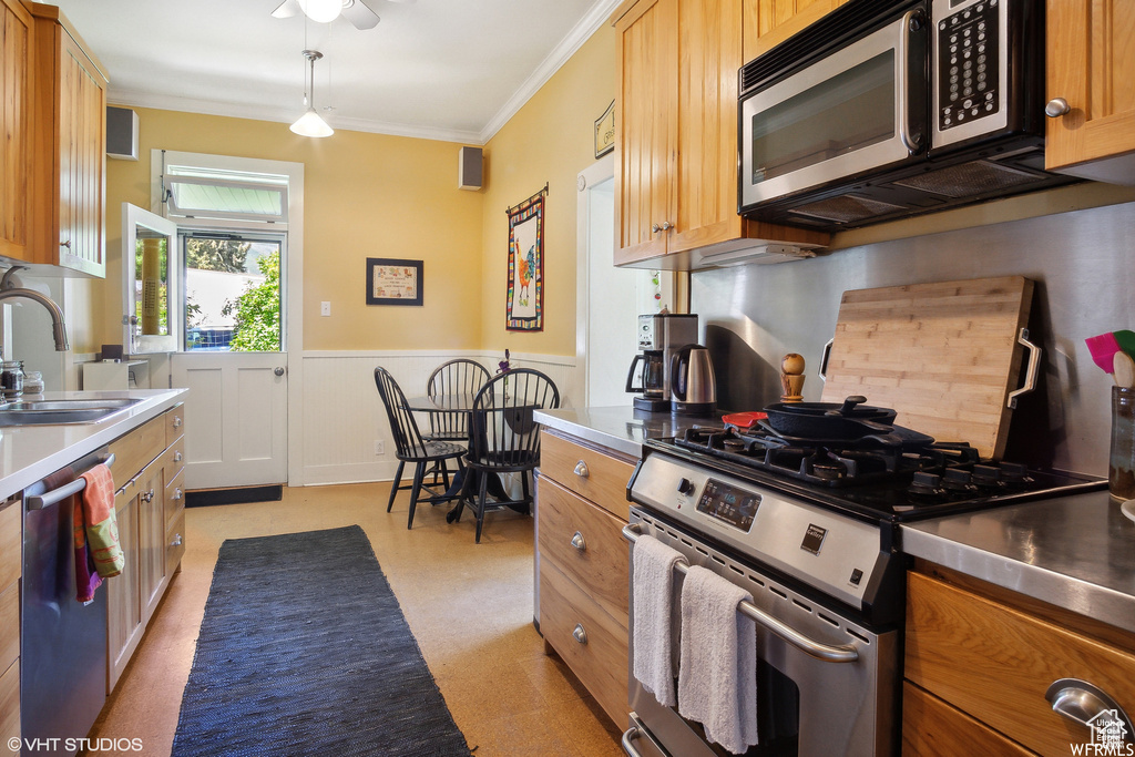Kitchen with stainless steel appliances, stainless steel countertops, a sink, a wainscoted wall, and ornamental molding