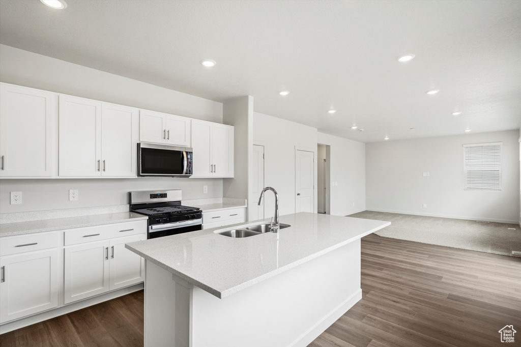 Kitchen featuring stainless steel appliances, white cabinetry, a center island with sink, open floor plan, and dark wood-type flooring