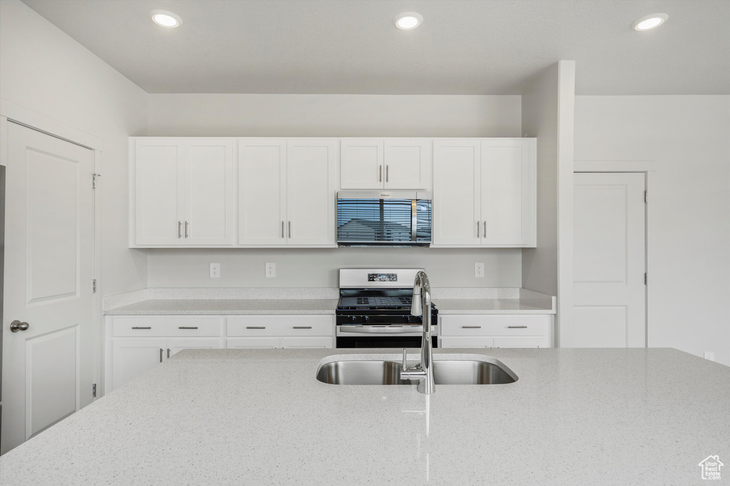 Kitchen featuring stainless steel appliances, white cabinetry, light stone countertops, and recessed lighting
