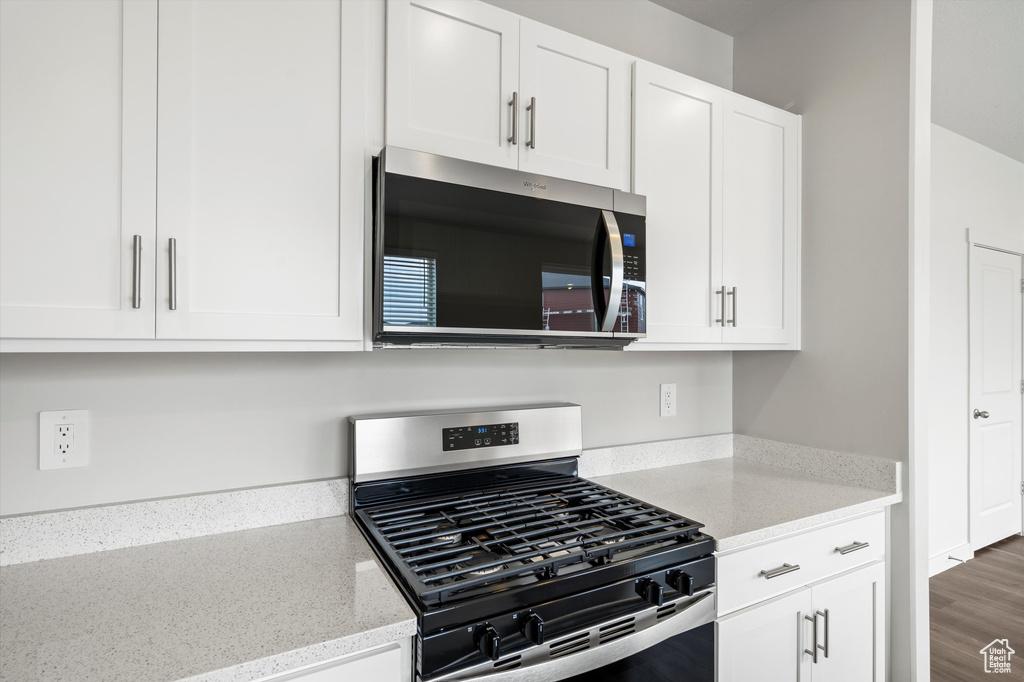 Kitchen with appliances with stainless steel finishes, white cabinets, and light stone counters