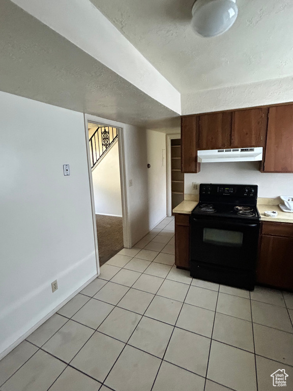 Kitchen featuring black / electric stove, light countertops, under cabinet range hood, light tile patterned flooring, and a textured ceiling