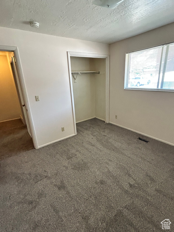Unfurnished bedroom featuring carpet floors, a closet, a textured ceiling, and baseboards