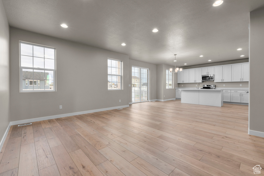 Unfurnished living room with baseboards, a chandelier, a sink, light wood-type flooring, and recessed lighting