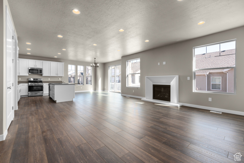 Unfurnished living room with a sink, a chandelier, recessed lighting, a glass covered fireplace, and baseboards